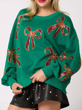 Emerald green oversized round neck sweatshirt with sparkling red sequin bow embellishments, care instructions recommend tumble dry low