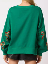 Emerald green oversized sweatshirt with sequin bow embroidery in red and gold and care instructions to tumble dry