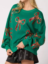 Emerald green oversized sweatshirt with sparkling red sequin bow accents and care instructions to tumble dry safely