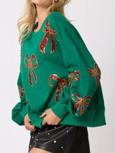 Emerald green oversized sweatshirt with shimmering red and gold sequin bow embellishments and care instructions to tumble dry