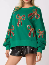 Emerald green oversized sweatshirt featuring sparkling red sequin bow embellishments with care instructions to tumble dry