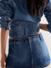 A mid-rise classic wash denim mini skort with visible stitching details in blue denim material