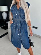 Blue denim sleeveless dress with white buttons and belted waist featuring collared neck cap sleeve design