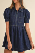 A navy blue denim dress with collared neck half zip, front zipper, and two patch pockets in denim material