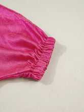 A vibrant pink velvet pant leg with a gathered ruffled hem paired with a collared v neck half sleeve metallic top