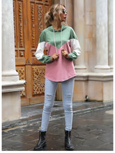 A woman wears a color block casual long sleeve hoodie in green white and pink made of slightly stretchy soft fabric machine wash