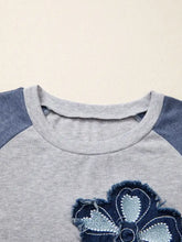 Gray and blue denim raglan sleeve top features embroidered distressed floral patch on front in casual long sleeve design