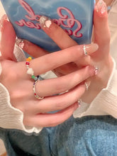 Manicured hands holding light blue phone with colorful acrylic beaded heart ring