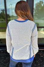 A woman wears a white and blue houndstooth contrast stitching round neck sweatshirt with ribbed cuffs and care instructions