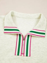 A cream-colored polo shirt with a zip collar featuring bold green and magenta striped patchwork zip details along the placket and collar edges