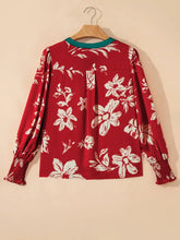 Red floral blouse with white blossoms and green trim featuring contrast tied neck and shirred puff sleeves with elastic cuffs