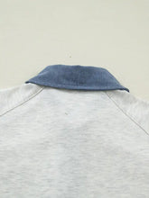 A light gray heathered white polo with contrast trim button detail and a blue denim collar for casual wear