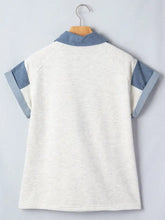 A heathered white polo with contrast trim button detail and denim blue collar and sleeve cuffs