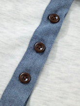 Three dark brown contrast trim buttons on blue denim fabric detail of a heathered white polo top