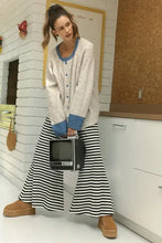 Woman in relaxed fit raglan sleeve cardigan with contrast trim button, striped pants, clogs, holding vintage TV