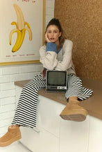 Woman in relaxed fit raglan sleeve cardigan with contrast trim button, striped pants, boots