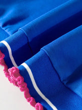 Vibrant royal blue short sleeve athletic sweatshirt with white stripes and playful pink pom trim on cuffs