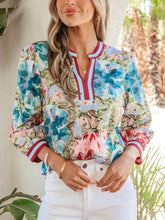 A vibrant floral blouse with v-neck, red and white striped trim, puffed sleeves, and cuffed bracelet sleeves