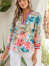A woman wears a light blue floral blouse with pink and teal roses and red white navy contrast trim