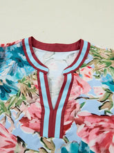 A vibrant floral blouse featuring a v-neckline with bold red and light blue striped contrast trim