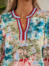 A woman wears a light blue floral blouse with a contrast trim v neck and cuffed bracelet sleeves