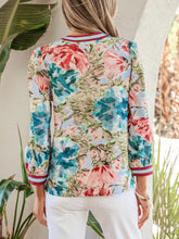 A floral blouse with contrast trim v neck cuffed bracelet sleeves featuring bold pink and teal blossoms on light blue