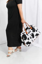 Cow print plush weekender bag with brown leather handles and gold hardware
