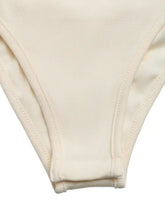 Cream-colored ribbed fabric bikini bottom with stitched seams paired with a cowl neck sleeveless bodysuit