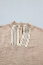 A beige linen pullover rolled short sleeve blouse with v-neckline, cream crochet lace accent, and vertical striped fabric