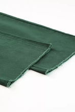 Dark green denim crossed waist raw hem shift jeans fabric with frayed edges showing texture and detail