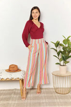 Woman wearing a maroon culture code full size v neck bodysuit paired with pastel striped high-waisted wide-leg pants