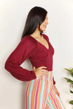 A woman wears a maroon satin culture code full size v neck bodysuit with ruched detailing and long sleeves