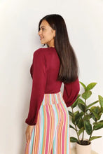 A woman wearing a culture code maroon satin full size v neck bodysuit paired with pastel striped wide-leg pants