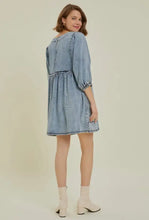 A light blue denim dress with cutout round neck, balloon sleeves, three-quarter length sleeves, and ruffled hem