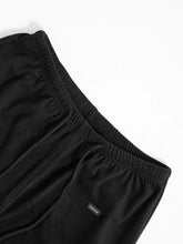 Black relaxed fit drawstring pants with elastic waist and subtle fashion label on the side seam