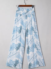 White wide-leg tropical print shirred waistband pants with blue tropical leaf pattern and flowing fabric