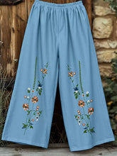 Light blue floral wide leg pants with intricate orange white and green blossom embroidery along the sides