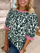 A woman wears a green and white damask print half sleeve blouse with pink ruffled color block trim at neckline and sleeves