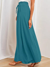 Teal-colored flowing wide leg pants with elastic waistband and drawstring featuring pockets for comfortable wear