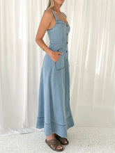 A light blue denim dress with thin straps front button closure and side pockets in a-line denim style