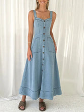 A light blue denim dress with thin straps, front button closure, and two patch pockets in a-line denim style