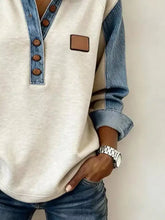 Cream-colored sweatshirt with denim trim on collar sleeves and button placket featuring brown buttons and tan leather patch