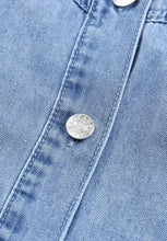 Silver circular button with embossed text on light blue denim fabric of distressed collared neck flounce denim dress
