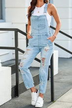 Distressed denim overalls with light wash rips and white sneakers