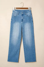 Light-wash blue denim tummy control raw hem jeans with subtle pattern and straight-leg cut hanging on wooden hanger