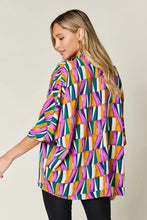 A vibrant oversized double take full size geometric notched dolman sleeve top in purple green orange and white perfect for jeans size styling