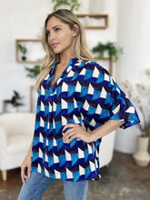A woman wears a blue and white double take full size geometric notched half sleeve blouse with short flared sleeves