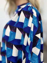 A woman wearing a double take full size geometric notched half sleeve blouse in vibrant blue white and black textured fabric