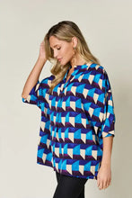 A woman wearing a double take full size geometric notched half sleeve blouse with blue white and purple patterns