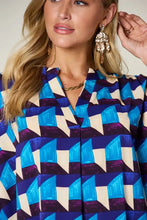 A woman wears a double take full size geometric notched half sleeve blouse with bold blue purple and cream tones